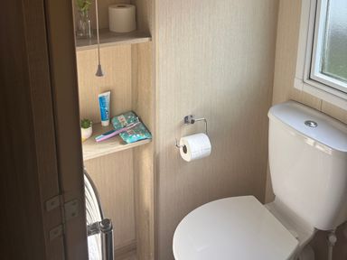 A bathroom with a toilet and shelf containing toiletries at Southview Holiday Park - Holiday Accommodation 19123, Skegness