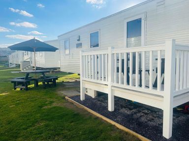 An outdoor area with a caravan, deck, table, and umbrella at Presthaven Beach Resort - Holiday Accommodation 19166 Prestatyn