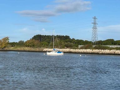 a sailboat on water near a rocky shore with trees and power lines at Rockley Park - Holiday Accommodation 19386, Poole
