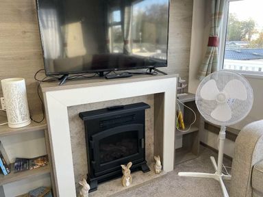 a television above a fireplace with decorative items and a fan at Rockley Park - Holiday Accommodation 19386, Poole