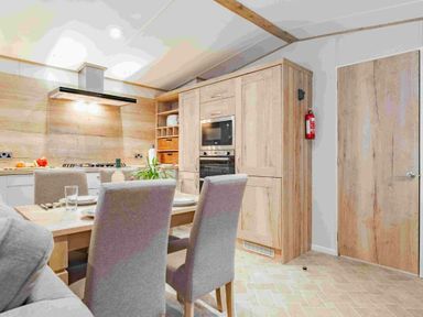 a kitchen and dining area with wooden cabinets and a table at Kelling Heath Holiday Park - Holiday Accommodation 19669, Holt