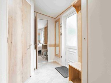 a hallway with a door, mirror, mat, and a bench at Kelling Heath Holiday Park - Holiday Accommodation 19669 in Holt