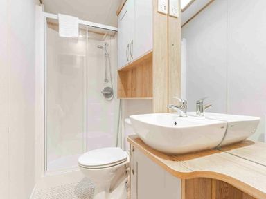 a bathroom with a shower, toilet, and sink with wooden cabinetry at Kelling Heath Holiday Park - Holiday Accommodation 19669, Holt