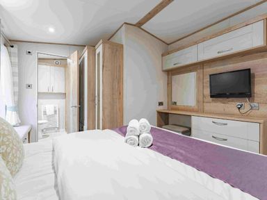 a bedroom with a bed, towels arranged, wardrobe, and a television at Kelling Heath Holiday Park - Holiday Accommodation 19669 in Holt