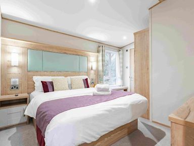 a bedroom with a large bed and wood accents at Kelling Heath Holiday Park - Holiday Accommodation 19669, Holt