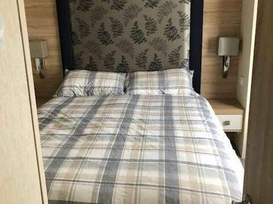 a bedroom with a checked bedspread and two pillows at Pinewoods Holiday Park - Holiday Accommodation 19734 in Wells-Next-The-Sea