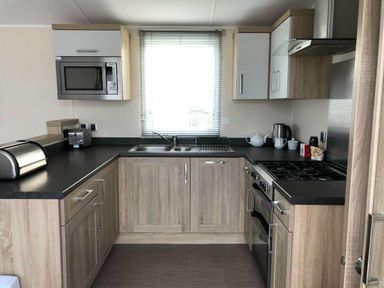 a kitchen featuring cabinets, a sink, a stove, and a microwave at Pinewoods Holiday Park - Holiday Accommodation 19734, Wells-Next-The-Sea