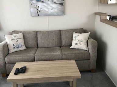 a living room with a grey sofa and a wooden coffee table at Pinewoods Holiday Park - Holiday Accommodation 19734, Wells-Next-The-Sea