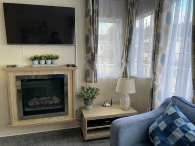 a living room with a TV, electric fireplace, and furniture at Pinewoods Holiday Park - Holiday Accommodation 19734 Wells-Next-The-Sea