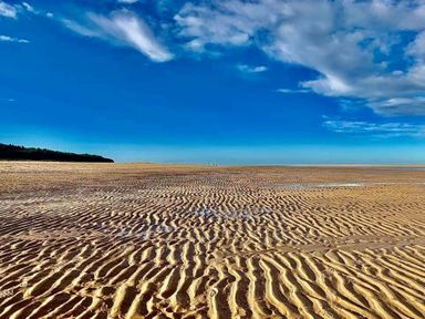 a sandy beach with rippled patterns under a blue sky at Pinewoods Holiday Park - Holiday Accommodation 19734 Wells-Next-The-Sea