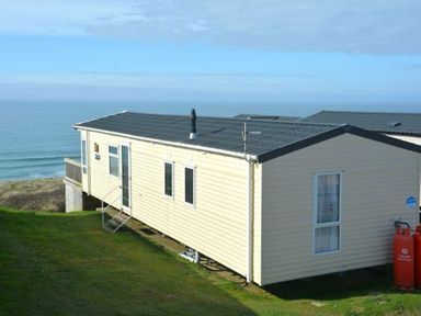 a holiday home with a grassy area and ocean view at Perran Sands - Holiday Accommodation 19778 Perranporth