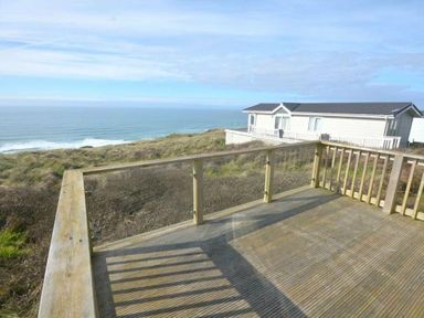 a deck with a view of the ocean and a building in the background at Perran Sands - Holiday Accommodation 19778 Perranporth