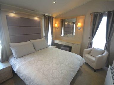 a bedroom with a double bed and a mirror with a chair and curtains at Perran Sands - Holiday Accommodation 19778 in Perranporth