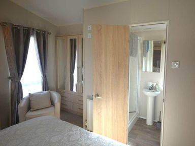 a bedroom with a chair, wardrobe, and connected bathroom at Perran Sands - Holiday Accommodation 19778 in Perranporth