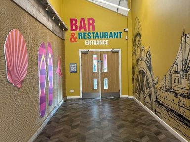 a hallway with colorful wall art and double doors leading to the bar and restaurant at Sand Le Mere Holiday Village - Holiday Accommodation 20326, Tunstall