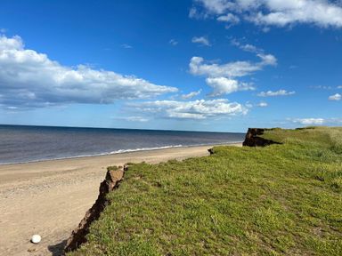 a beach with a cliff and grass in the foreground at Sand Le Mere Holiday Village - Holiday Accommodation 20326 Tunstall