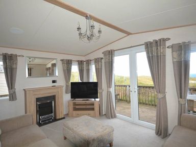 a living room with a sofa, television, chandelier, and doors leading to an outdoor area at Perran Sands - Holiday Accommodation 20514, Perranporth
