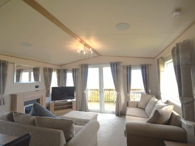 a living room with a television, sofa, and large windows at Perran Sands - Holiday Accommodation 20514, Perranporth