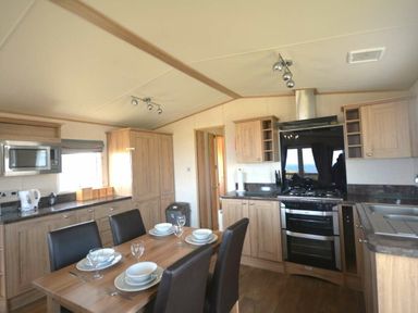 a kitchen and dining area with wooden cabinets and a dining table at Perran Sands - Holiday Accommodation 20514 Perranporth