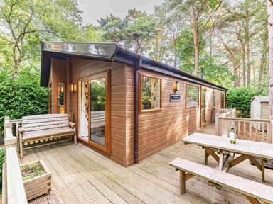 a wooden cabin with a deck and outdoor seating at Kelling Heath Holiday Park - Holiday Accommodation 20952 in Weybourne