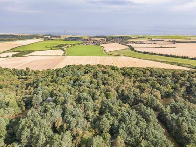 an aerial view of fields and trees with a village near the coast at Kelling Heath Holiday Park - Holiday Accommodation 20952 in Weybourne