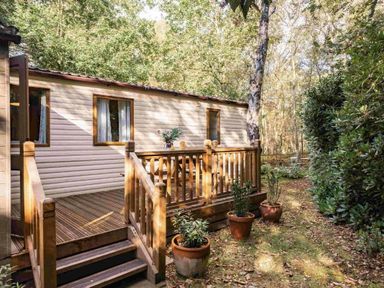 a holiday cabin with a wooden deck and potted plants at Kelling Heath Holiday Park - Holiday Accommodation 20958 in Weybourne