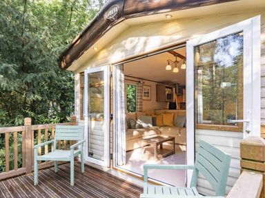 a deck with two chairs leading to a cabin with large windows at Kelling Heath Holiday Park - Holiday Accommodation 20958 Weybourne