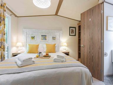 a bedroom with a double bed, bedside tables, lamps, and a wooden wardrobe at Kelling Heath Holiday Park - Holiday Accommodation 20958, Weybourne