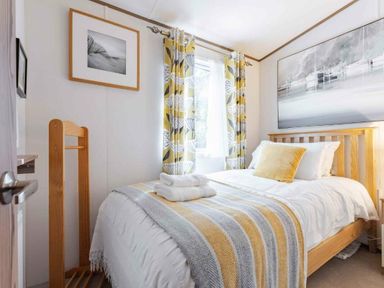 a bedroom with a bed, wooden furniture, and patterned curtains at Kelling Heath Holiday Park - Holiday Accommodation 20958, Weybourne