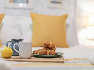a tray with croissants, a cup, a small pitcher, and a lemon on a bed with yellow cushions at Kelling Heath Holiday Park - Holiday Accommodation 20958 in Weybourne