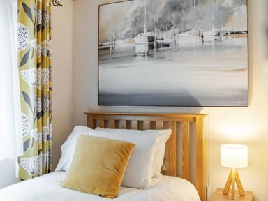a bedroom with a wooden headboard, white bedding, a yellow pillow, and a painting of boats on the wall at Kelling Heath Holiday Park - Holiday Accommodation 20958, Weybourne