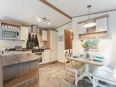 a kitchen with cabinets, a dining table, and appliances at Kelling Heath Holiday Park - Holiday Accommodation 20958, Weybourne