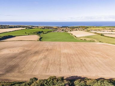 an aerial view of fields and a coastal village with the sea in the background at Kelling Heath Holiday Park - Holiday Accommodation 20958, Weybourne