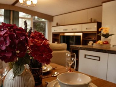 a dining table with flowers and dinnerware at Kelling Heath Holiday Park - Holiday Accommodation 21026 in Kelling Heath