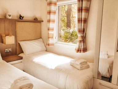 a bedroom with two single beds and a window with curtains at Kelling Heath Holiday Park - Holiday Accommodation 21026 in Kelling Heath