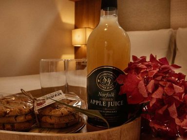 a bottle of apple juice with two glasses and cookies on a tray at Kelling Heath Holiday Park - Holiday Accommodation 21026 Kelling Heath