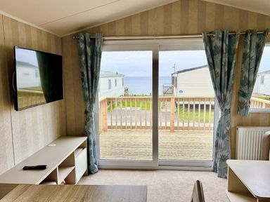 a living room with a TV and curtains overlooking a balcony at Perran Sands - Holiday Accommodation 21088 in Perranporth