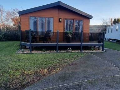 a cabin with a wooden deck surrounded by grass at Presthaven Beach Resort - Holiday Accommodation 21358 in Prestatyn