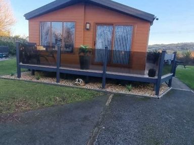 a cabin with a deck and glass railing surrounded by grass at Presthaven Beach Resort - Holiday Accommodation 21358, Prestatyn