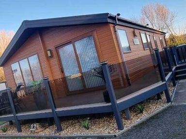 a wooden lodge with large windows and a deck area at Presthaven Beach Resort - Holiday Accommodation 21358, Prestatyn