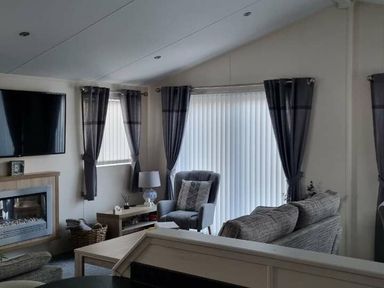 a living room with a television, curtains, and furniture at Presthaven Beach Resort - Holiday Accommodation 21358 in Prestatyn