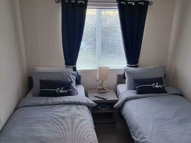 a bedroom with two twin beds and a window with curtains at Presthaven Beach Resort - Holiday Accommodation 21358 in Prestatyn