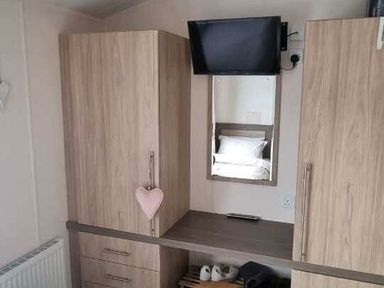 a wooden storage unit with a TV mounted above a mirror at Presthaven Beach Resort - Holiday Accommodation 21358, Prestatyn