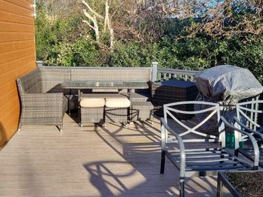 an outdoor patio area with a rattan seating set, a glass table, and a barbecue at Presthaven Beach Resort - Holiday Accommodation 21358, Prestatyn