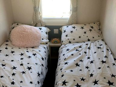 a bedroom with two beds featuring star-patterned bedding and a small table with a rainbow decoration at Greenacres Holiday Park - Holiday Accommodation 21467 Morfa Bychan