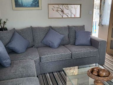 a gray sectional sofa with pillows and a glass coffee table at Swanage Bay View - Holiday Accommodation 21567 in Swanage