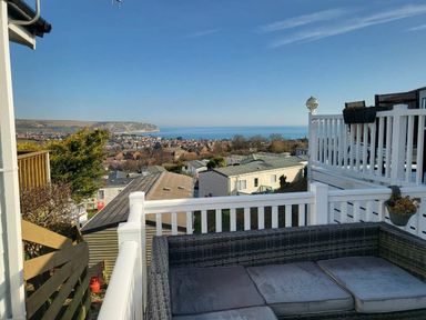 a view of the sea and town from a balcony with outdoor seating at Swanage Bay View - Holiday Accommodation 21567 in Swanage