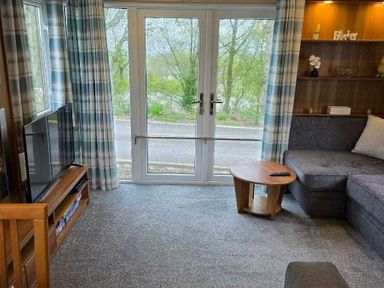 a living room with a gray sofa, wooden furniture, and large windows at Beacon Fell View Holiday Park - Holiday Accommodation 21653 Preston