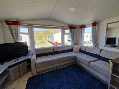 a living room with a corner sofa and a television at Clarach Bay Holiday Village - Holiday Accommodation 21674 in Aberystwyth