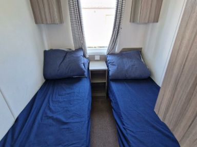 a bedroom with two single beds, a bedside table, and a window at Clarach Bay Holiday Village - Holiday Accommodation 21674, Aberystwyth